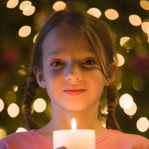 Girl with candle in from of Christmas tree